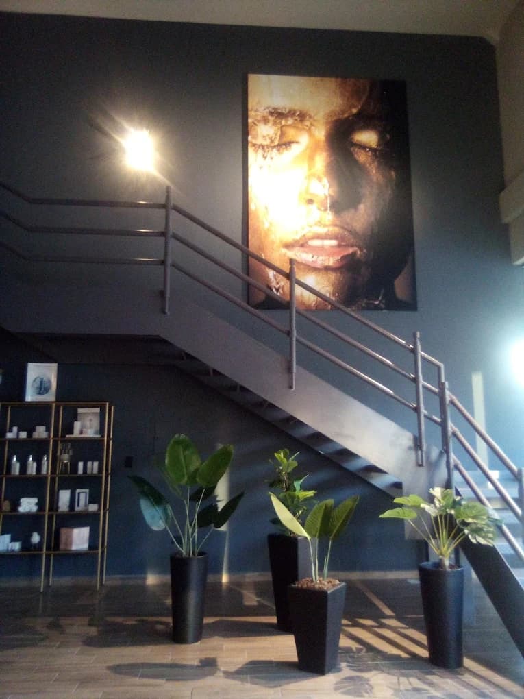 Retrato dorado de un rostro en pared gris junto a escalera metálica y plantas verdes.
